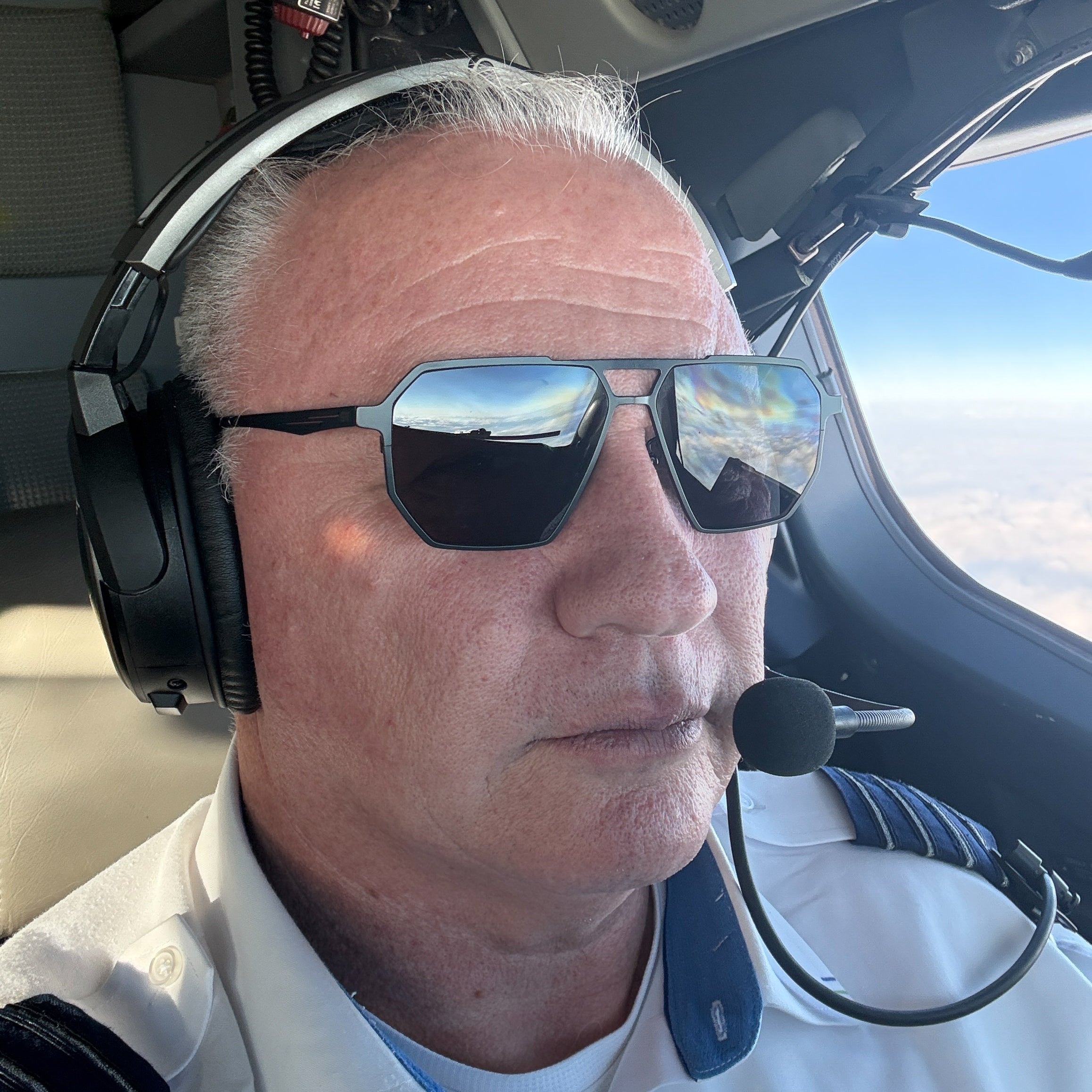 Man wearing Skyrift sunglasses and a headset inside an airline cockpit.