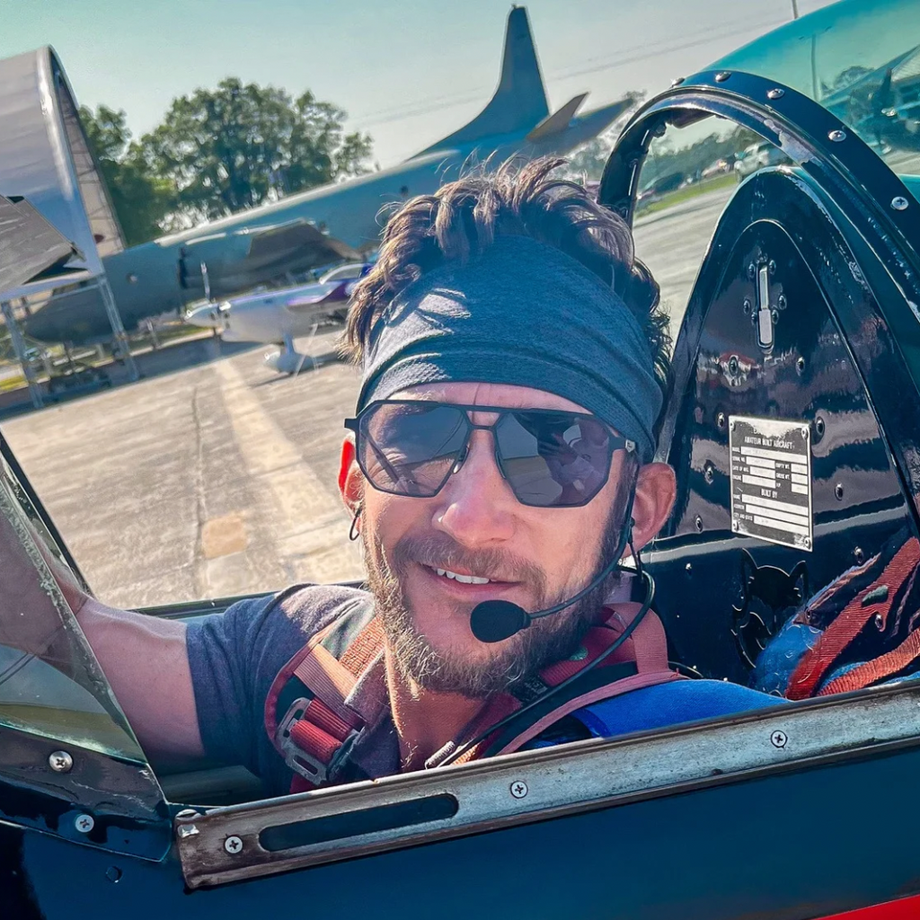 Pilot in SR Performance Eyewear vector sunglasses and a headset inside a small airplane cockpit with another airplane in the background.